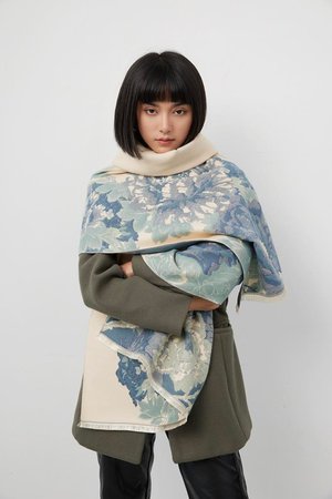 Woman wearing a luxurious soft blue and cream reversible wrap, showcasing elegant floral patterns and stylish layering.