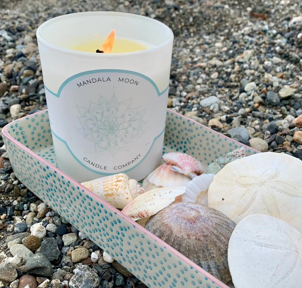Candle with 'Mandala Moon' label on pebbles and shells