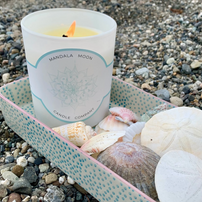 Candle with 'Mandala Moon' label on pebbles and shells