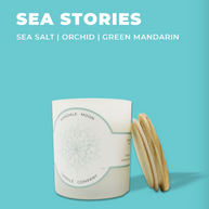 Candle with wooden lid on a light blue background, featuring 'Sea Stories' scents.